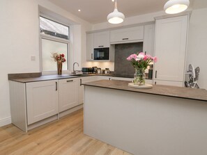 A modern kitchen with white cabinets, a central island, and a window with a view. - Park Beck (Windermere)