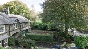 A stone house with a garden, a pond, and a fence.
