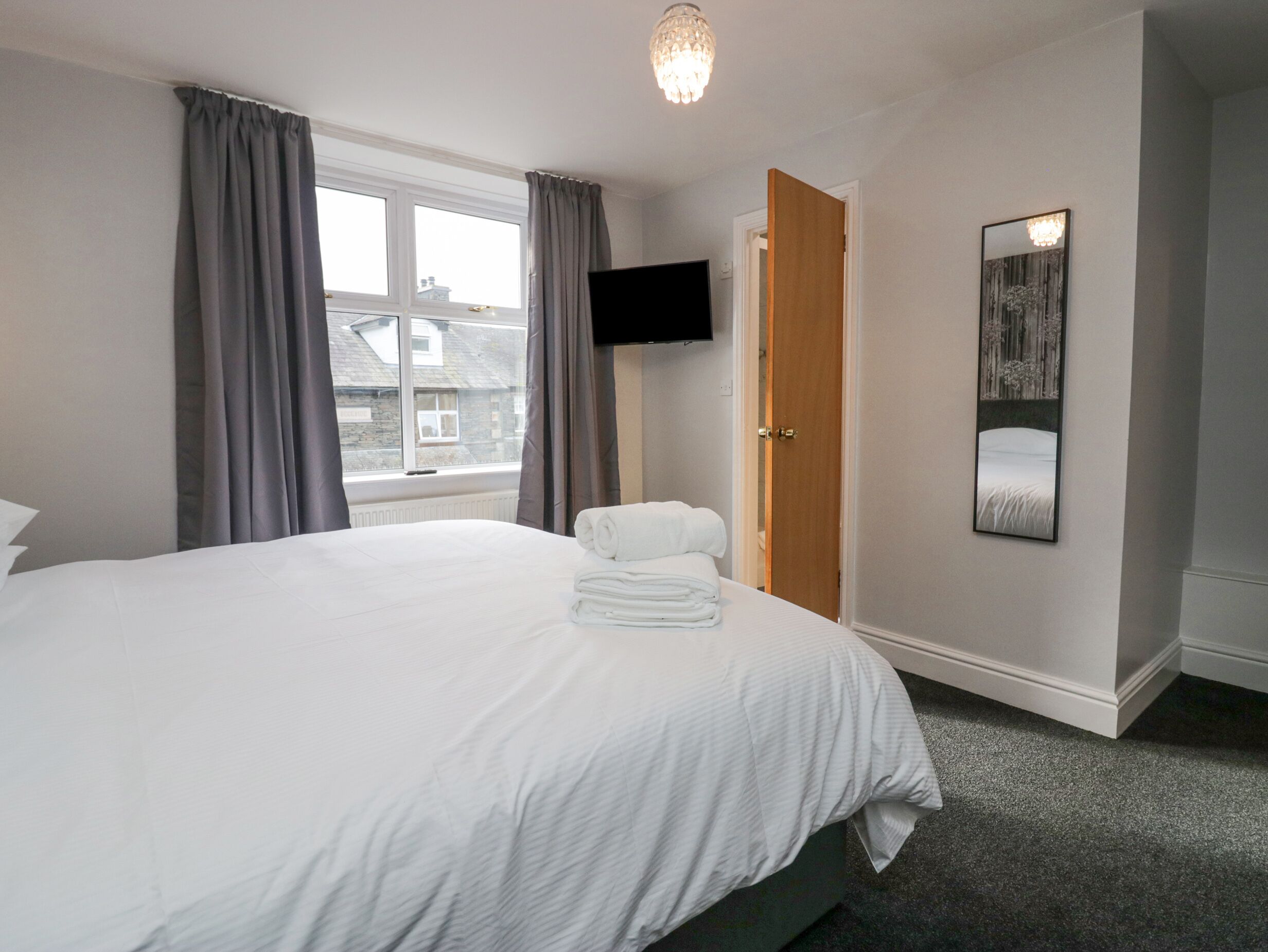 A hotel room with a large bed, a flat-screen TV mounted on the wall, and a view of buildings outside the window.