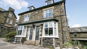 A two-story stone house with a bay window, a front door, and a small porch.