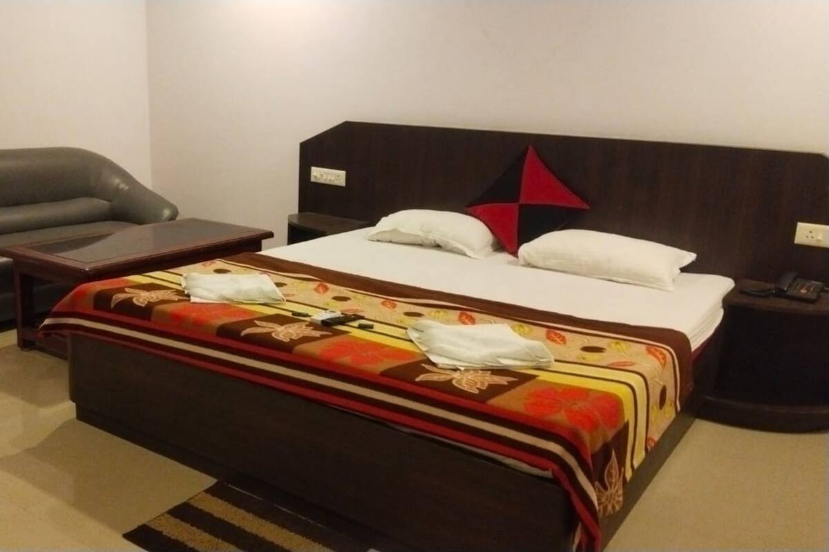 A hotel room with a bed, a sofa, a nightstand, and a wall-mounted TV.
