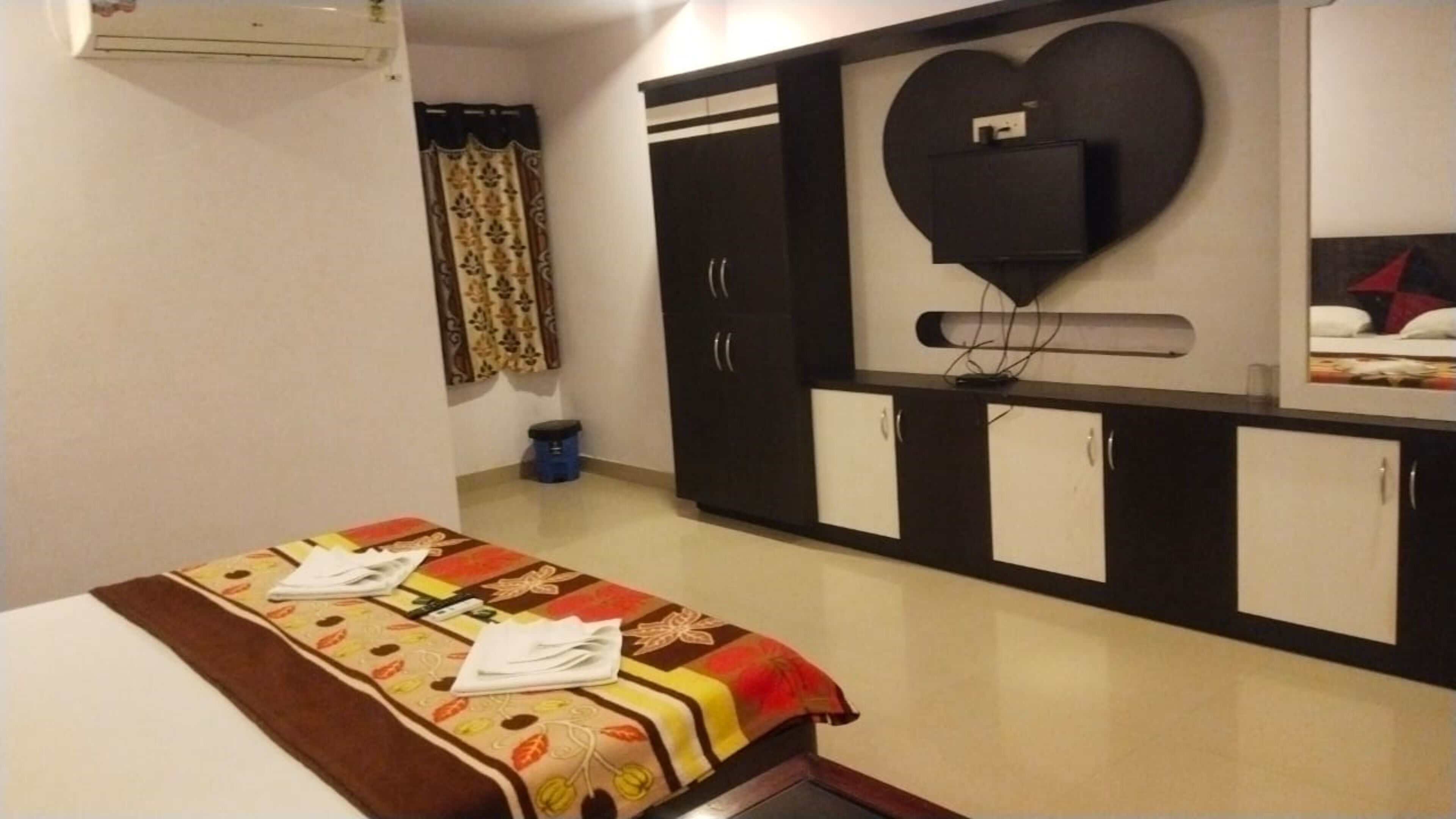 A hotel room with a bed, a wardrobe, a television mounted on the wall, and a small trash bin.