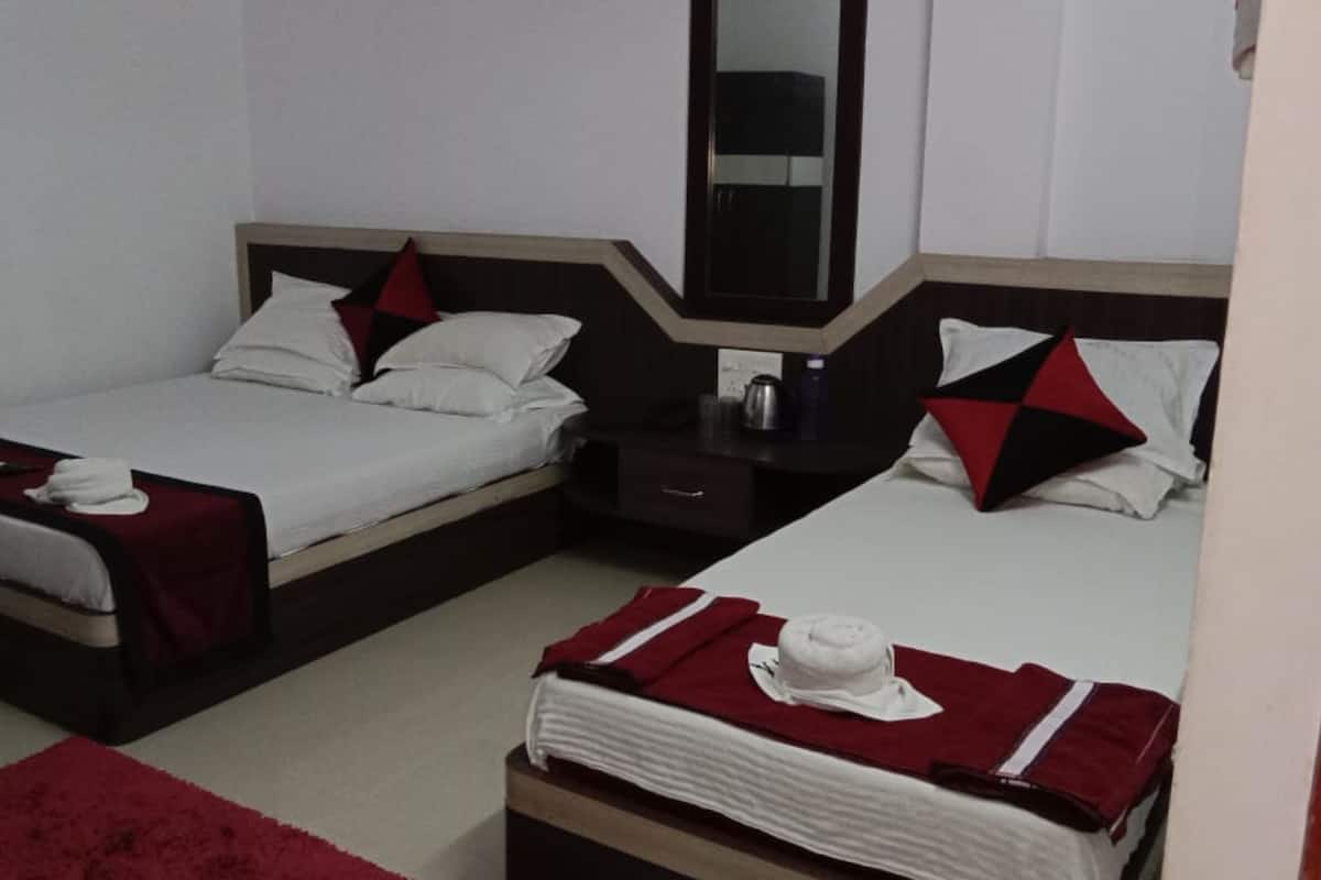 A hotel room with two single beds, each with a red and white pillow, a bedside table with a lamp, and a mirror above the bed.