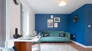 Ein modernes Wohnzimmer mit einem türkisfarbenen Sofa, einem Esstisch mit Stühlen, einem Couchtisch und einem großen Fenster.