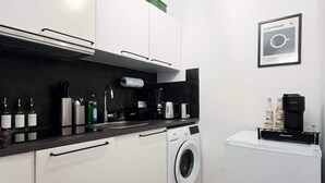Pieni, käytännöllinen keittiö, jossa on valkoiset kaapit, pesukone ja kahvinkeitin.