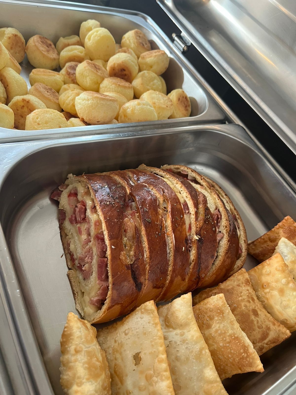 Buffet com variedade de alimentos, incluindo um prato grande de carne, batatas rústicas e salgados fritos.