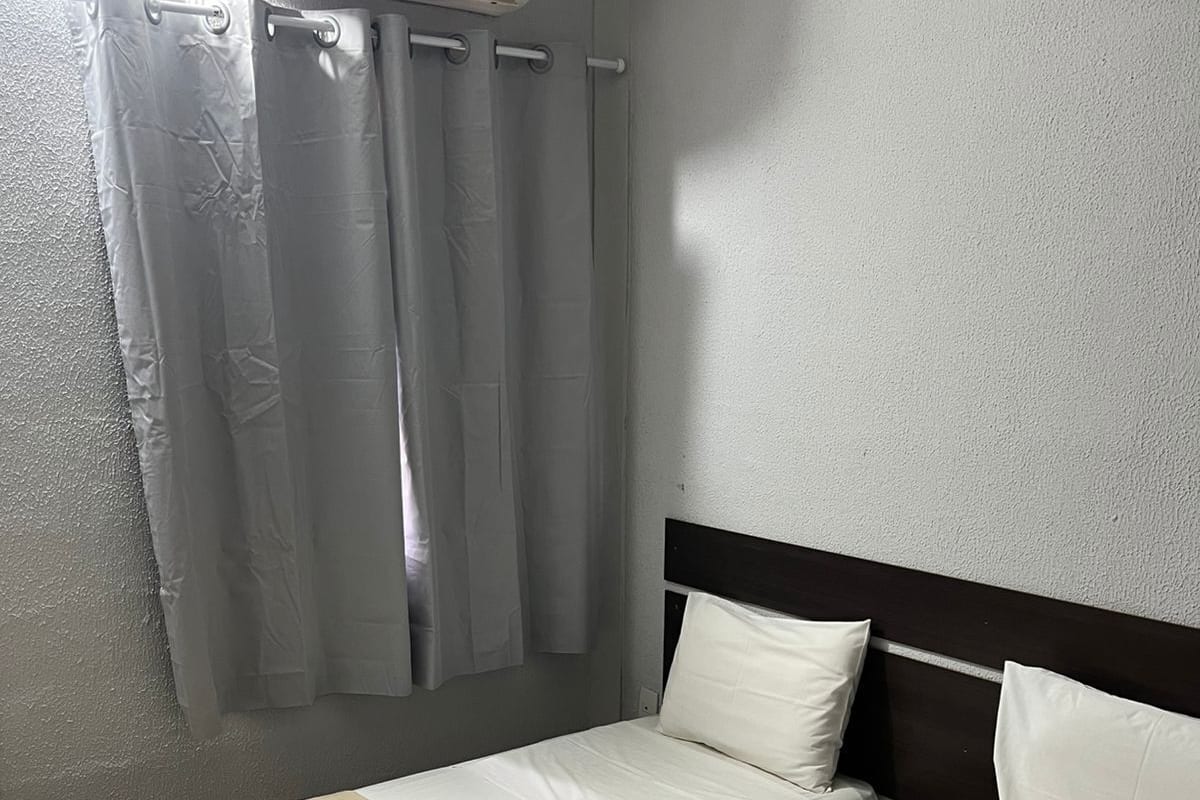 A hotel room with two single beds, a headboard, a window with curtains, and an air conditioning unit.