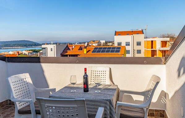 A balcony with a table set for two, overlooking a coastal area with buildings and solar panels. - Beach front home in Medulin with WiFi (Medulin)