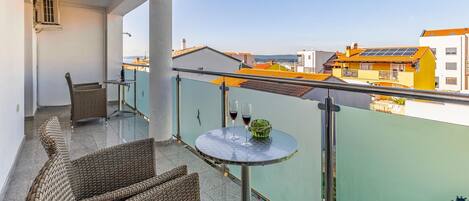 Varanda com móveis de vime, uma mesa com duas taças de vinho e vista para edifícios com telhados laranja.