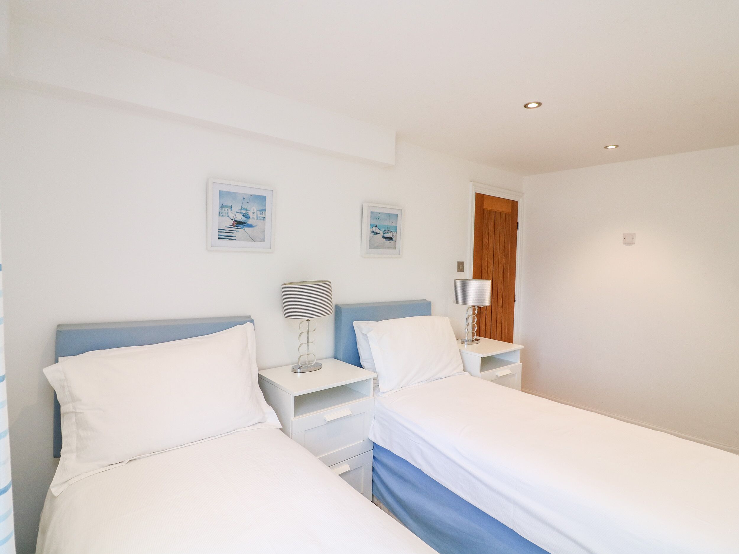 A hotel room with two beds, a nightstand with a lamp, and two framed pictures on the wall.