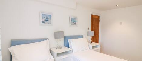 A hotel room with two beds, a nightstand with a lamp, and two framed pictures on the wall.