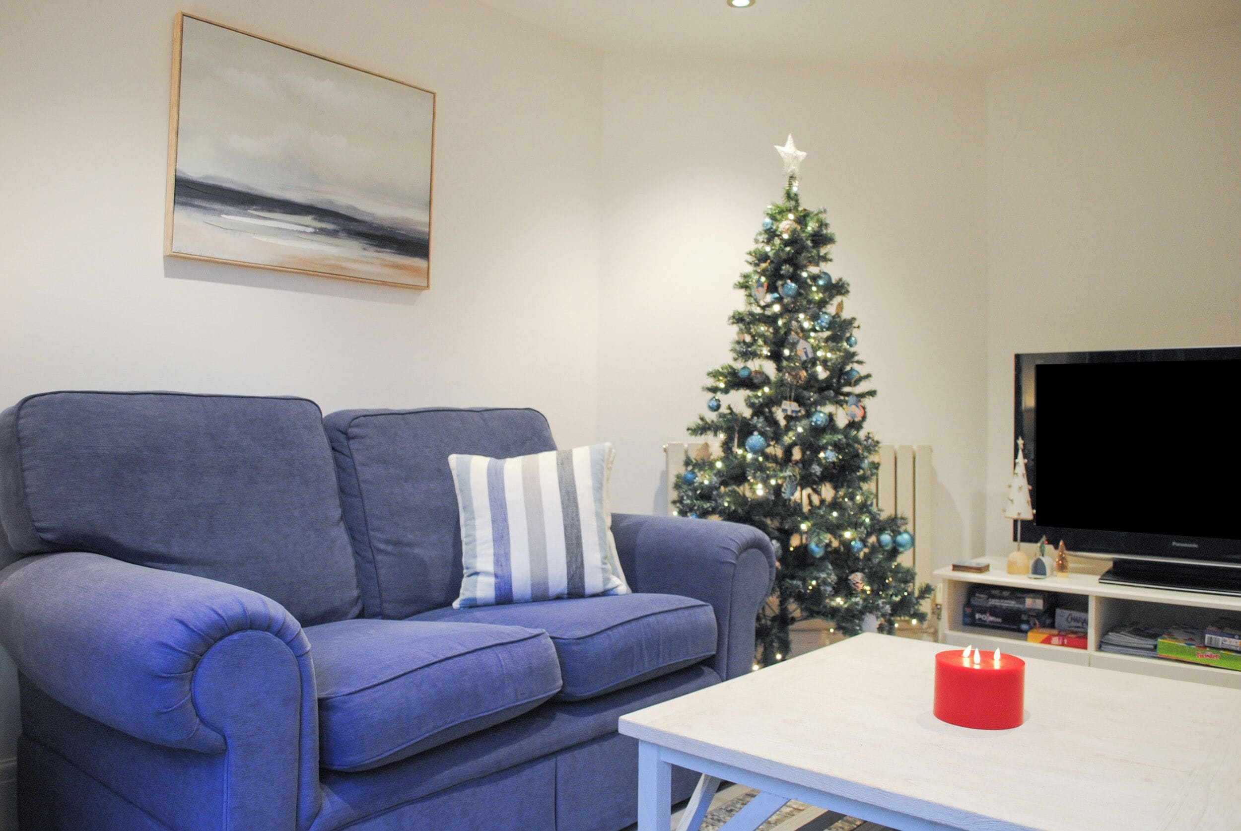 A living room with a blue sofa, a white coffee table, a Christmas tree, and a flat-screen TV.