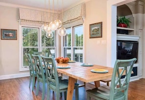 Une salle à manger avec une table en bois, des chaises vertes, un lustre et une cheminée.