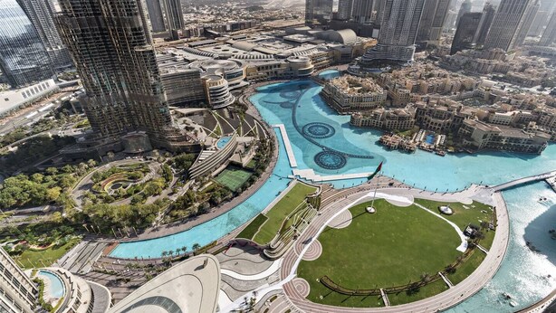 A high-rise urban area with modern architecture, a central water feature, and surrounding greenery.