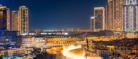 A cityscape at night with illuminated buildings and a central fountain.