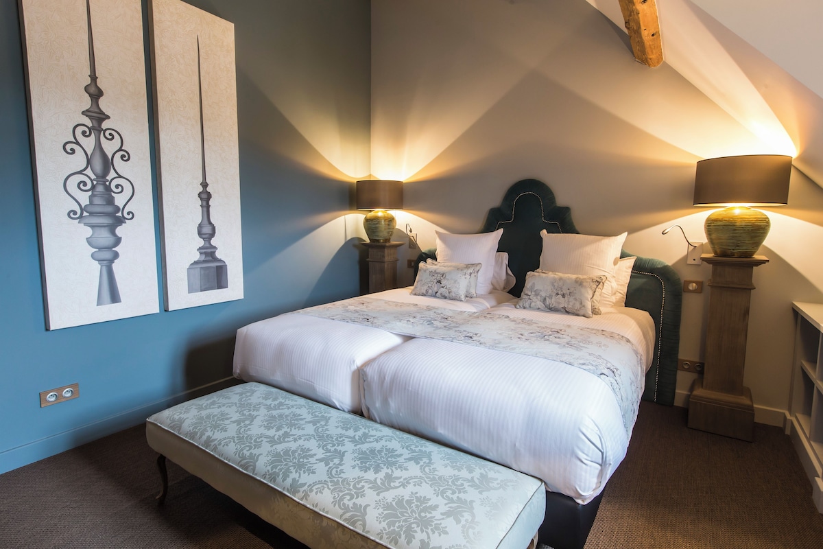 A bedroom with a large bed, two bedside lamps, a bench, and two wall-mounted picture frames.