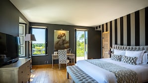 Un dormitorio con una cama grande, un escritorio, una silla, un televisor y una ventana con vistas al verdor.