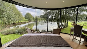 Un dormitorio con una cama grande, un escritorio y una silla, con vistas a un lago y vegetación.