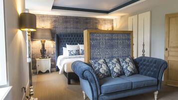 A bedroom with a bed, a blue sofa, a nightstand with a lamp, and a patterned wall.