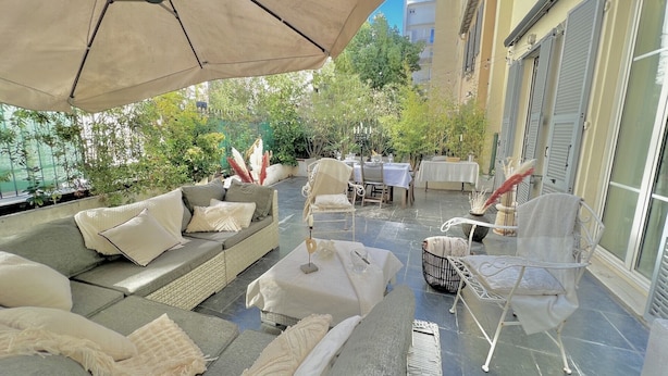 An outdoor patio with a covered seating area, including a sofa and chairs, and a table set for dining.