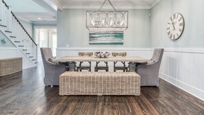 A dining area with a wooden table, grey upholstered chairs, a woven bench, a chandelier, and a wall clock. - Seagrove Beach Paradise: Salty Days - Your Dream 30A Getaway! (Santa Rosa Beach)