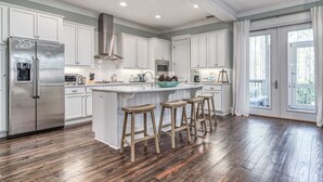 A spacious kitchen with white cabinets, a stainless steel refrigerator, wooden stools, and a large island. - Seagrove Beach Paradise: Salty Days - Your Dream 30A Getaway! (Santa Rosa Beach)