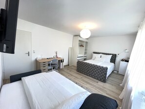 Une chambre d’hôtel moderne équipée de deux lits, d’un bureau, d’une armoire et d’une petite kitchenette.