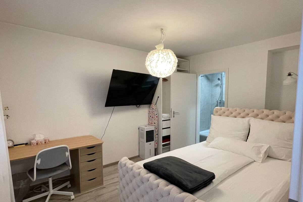 A bedroom with a bed, a desk, a chair, a TV, and a wardrobe.