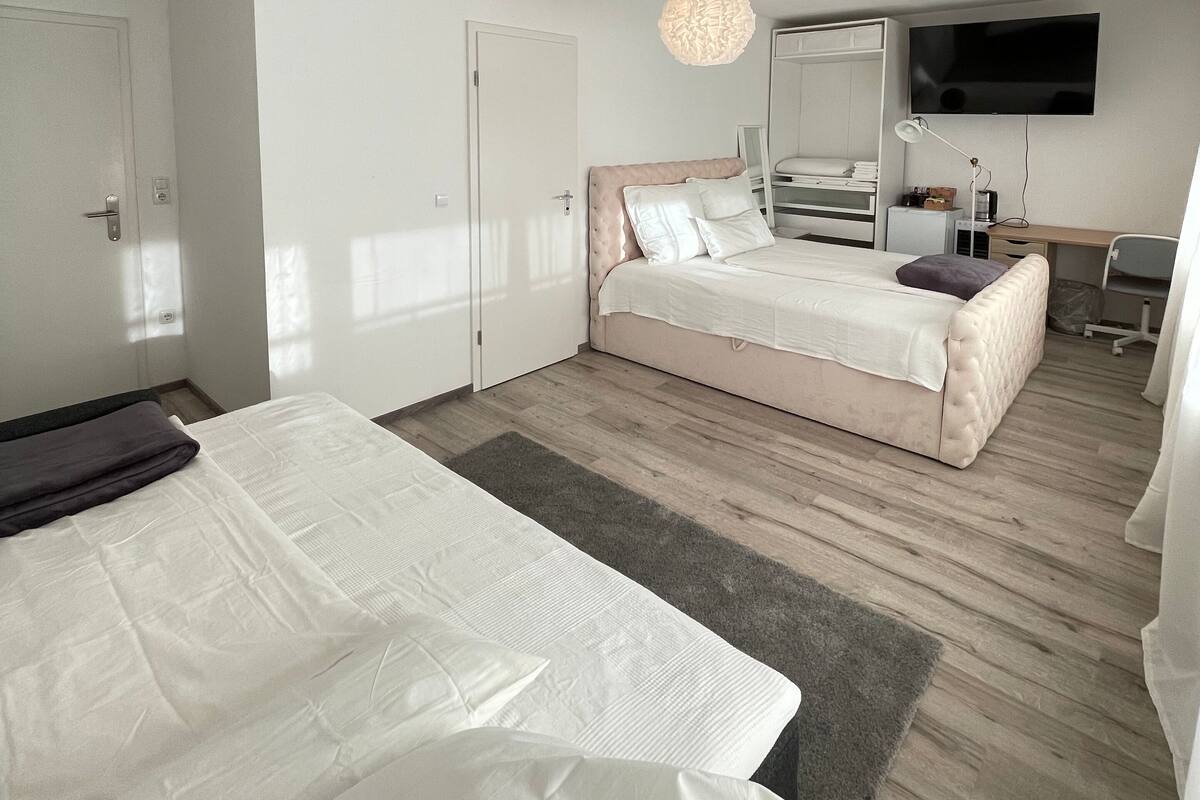A bedroom with a large bed, a smaller bed, a desk, a chair, a TV, and a wardrobe.