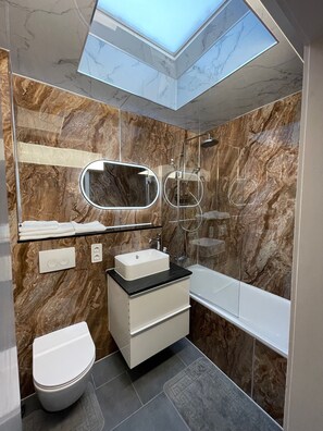 Une salle de bain moderne avec un puits de lumière, des murs en marbre, un lavabo blanc et une douche à parois de verre.