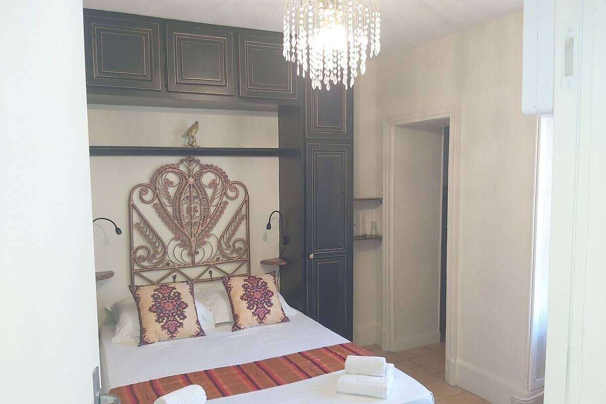 Una cama bien hecha con un tablero decorativo, una araña y una puerta a la derecha.