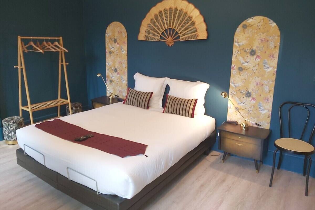 Una cama grande con estructura de madera, dos mesitas de noche, una silla colgante y un ventilador de pared.