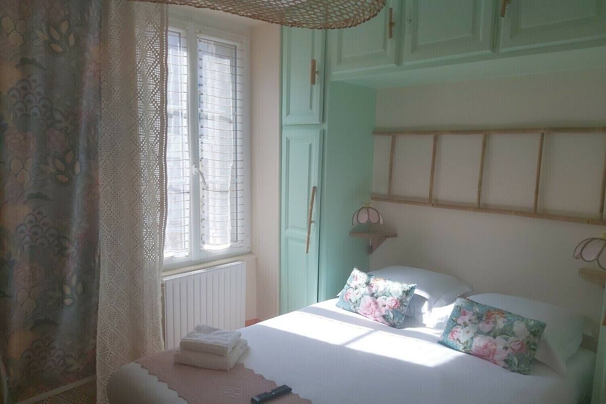 Un dormitorio con cama, una ventana con cortinas, un radiador y una mesita de noche con control remoto.
