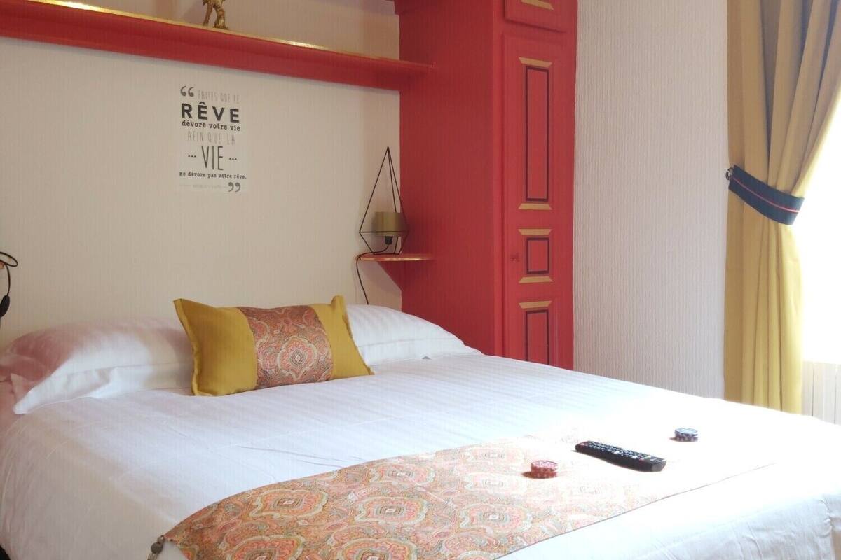 Habitación de hotel con una cama, una cita decorativa en la pared, una lámpara de noche y una ventana con cortinas.