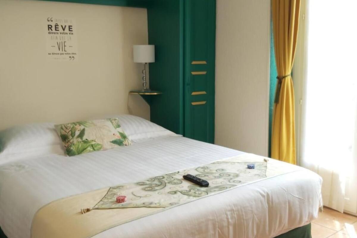 Una cama bien hecha con un cojín decorativo, un control remoto y una cita en la pared en francés.