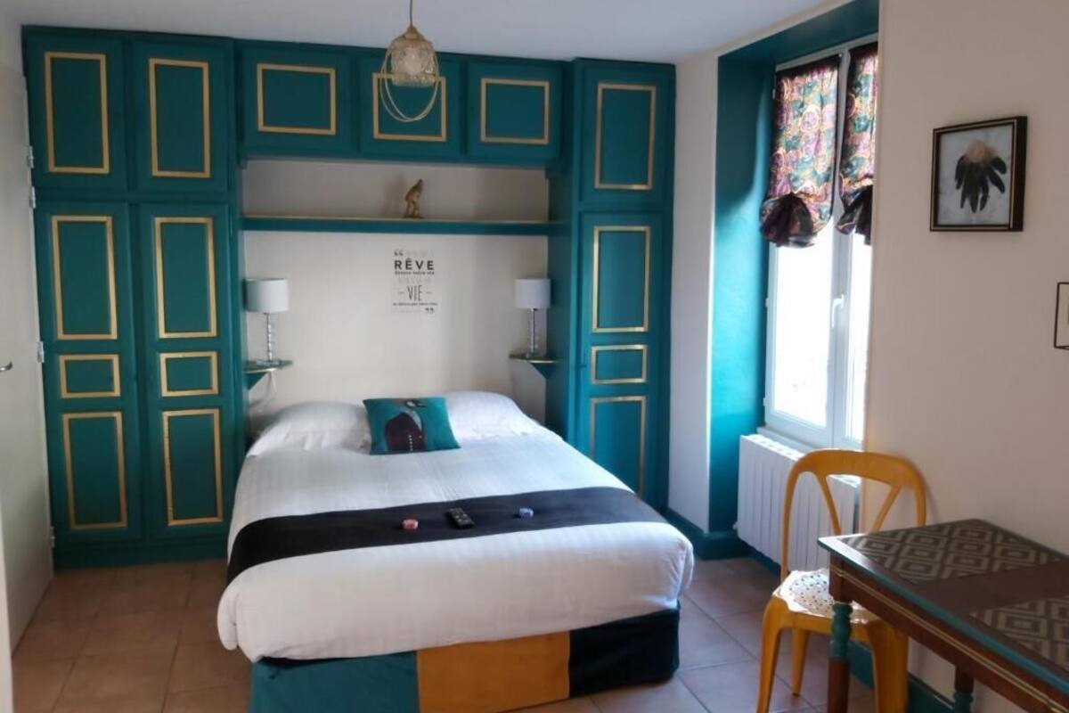 Un dormitorio con cama, escritorio y silla. Hay una ventana con cortinas y un cuadro en la pared.