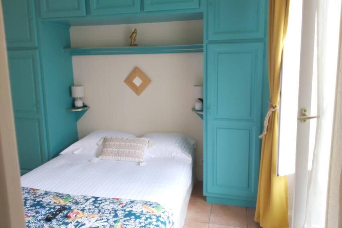 Un dormitorio con cama, paredes color turquesa, cabecero blanco y cortina amarilla.