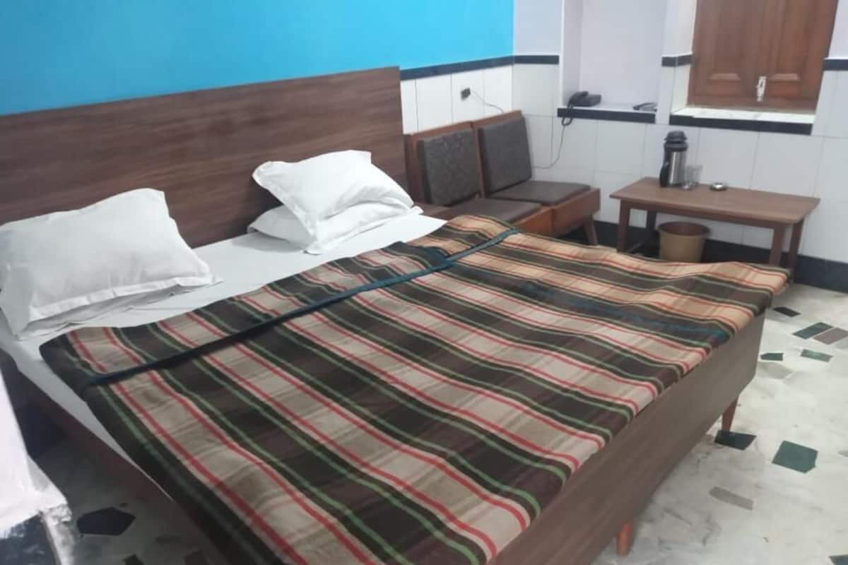 Un lit simple avec une couverture à rayures, une tête de lit en bois et une table de chevet avec une lampe.