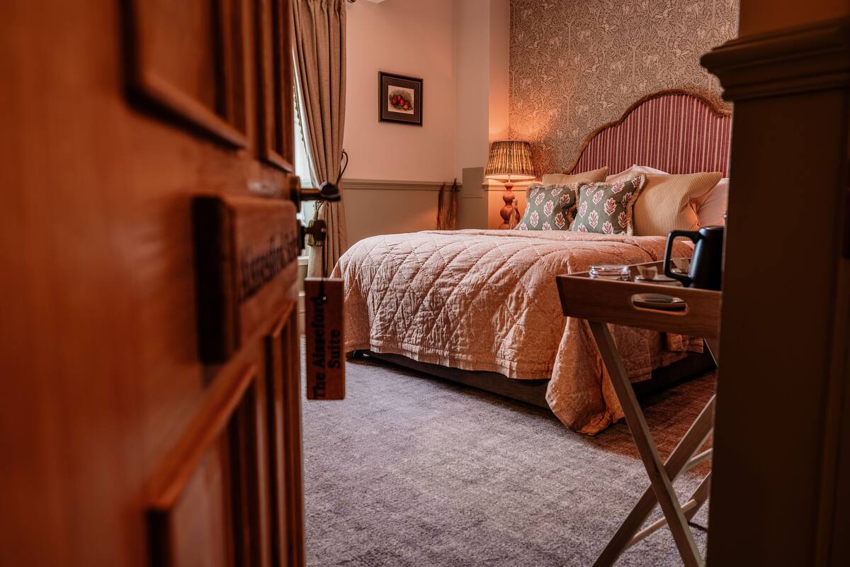 A bedroom with a bed, bedside table, lamp, and a framed picture on the wall.