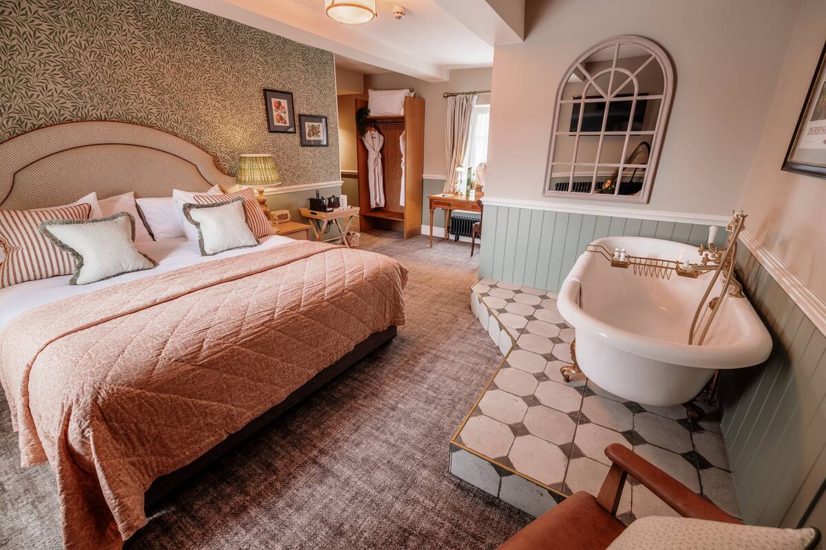 A bedroom with a large bed, a classic clawfoot bathtub, and a walk-in closet.