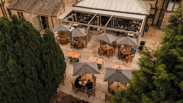 An outdoor patio with tables and chairs, surrounded by stone walls and trees. - The Ashford Arms (Bakewell)