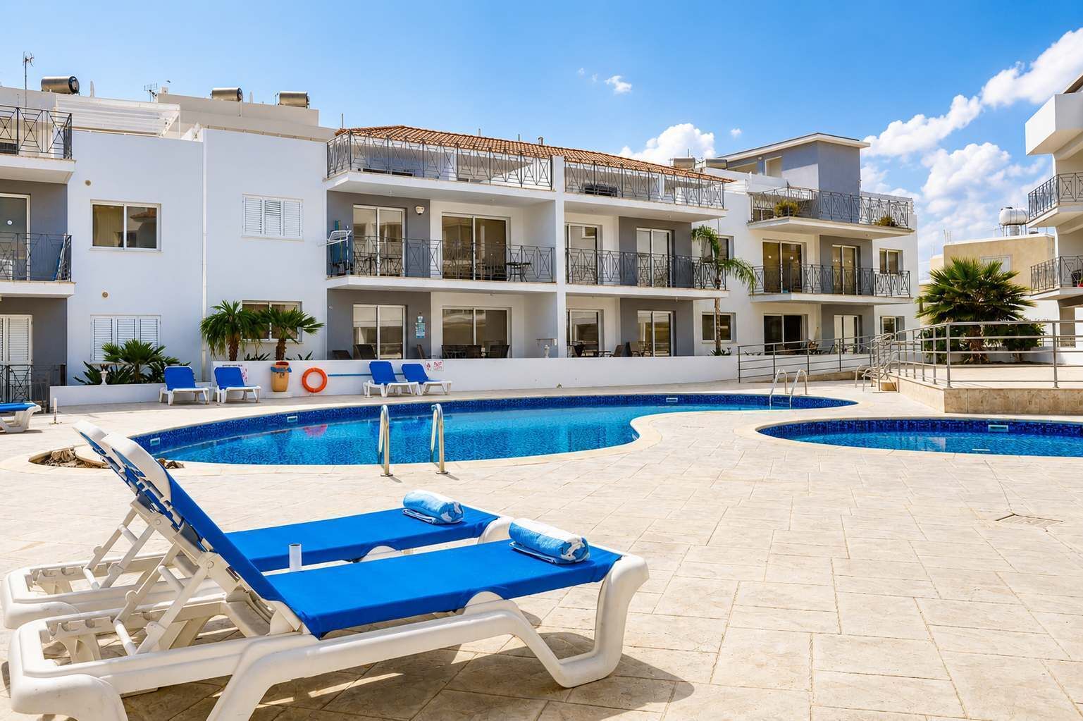 A swimming pool with lounge chairs, a lifebuoy, and a building with balconies.