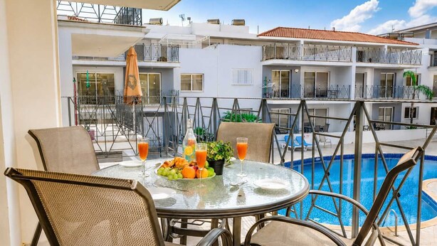 A poolside table with wicker chairs, a glass table, and a fruit platter with drinks. - 2BR Apartment with Pool - Poppy by Premier (Paralimni)
