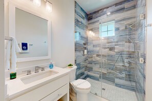 A modern bathroom with a large mirror, white vanity, and a glass shower enclosure with marble-like tiles. - Private Heated Pool, Resort Pools, Golf Cart Boardwalk to the Beach (Port Aransas)