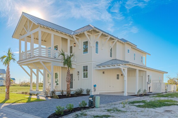 A large, two-story house with a covered porch, multiple windows, and a garage. - Private Heated Pool, Resort Pools, Golf Cart Boardwalk to the Beach (Port Aransas)