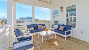 A covered outdoor seating area with a white ceiling, blue sofas, and a white coffee table.