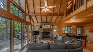 A spacious living room with a large gray sectional sofa, a stone fireplace, and a ceiling fan. - Turrach Ridge Retreat by Innsbrook Vacations! (Innsbrook)