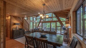 A spacious wooden dining area with a large table and chairs, a chandelier, and a view of the outdoors through large windows. - Turrach Ridge Retreat by Innsbrook Vacations! (Innsbrook)