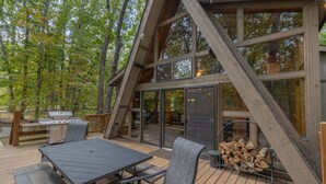 A wooden deck with a table and chairs, a grill, and a stack of firewood. - Turrach Ridge Retreat by Innsbrook Vacations! (Innsbrook)