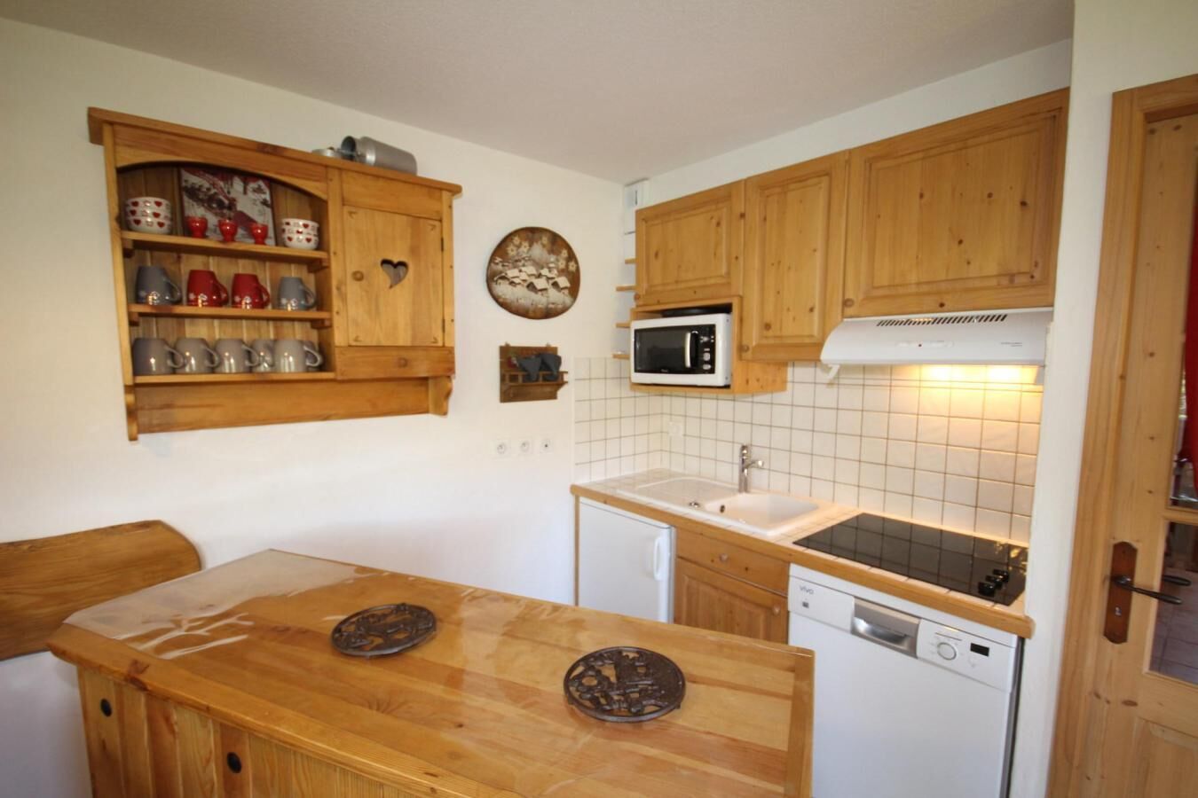 Een functionele keuken met houten kasten, een magnetron, een vaatwasser, en een klein eethoekje met een houten tafel en stoelen.